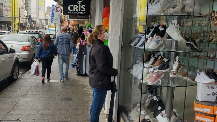 #ParaTodosVerem Na foto, um mulher olha para a vitrine de uma loja. Mais ao fundo, algumas pessoas caminham na calçada