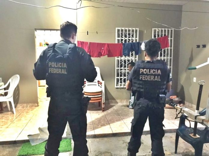 #ParaTodosVerem Na foto, dois policiais federais estão de costas em frente de uma casa, em Roraima, onde cumprem um mandado de busca e apreensão