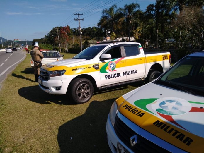 #ParaTodosVerem Na foto, um policial militar rodoviário faz uma consulta ao sistema durante a abordagem de um veículo. Ele está às margens de uma rodovia estadual onde também há duas viaturas paradas