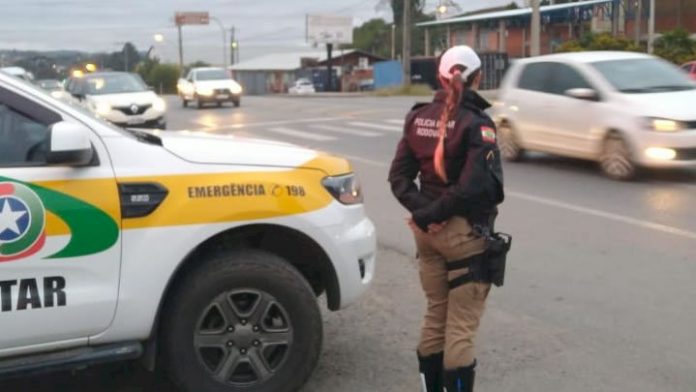 #ParaTodosVerem Na foto, uma policial militar rodoviária está ao lado de uma viatura, às margens de uma estrada, fiscalizando o trânsito