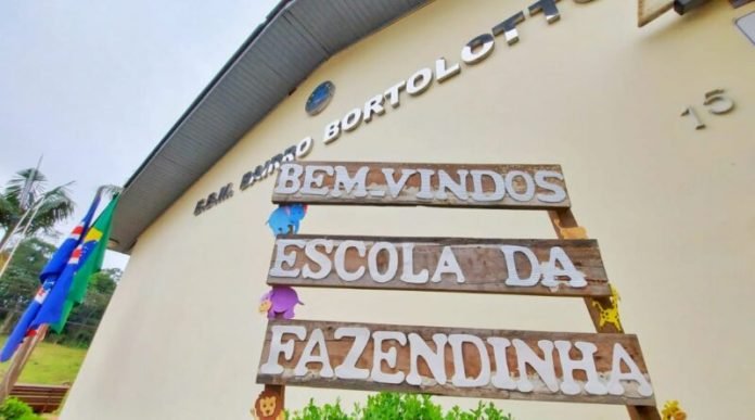 Rida da fazendinha #ParaTodosVerem Na foto, a fachada da Escola Escola Básica Municipal Bairro Bortolotto, em Nova Veneza. Na frente, há uma placa com os dizeres: