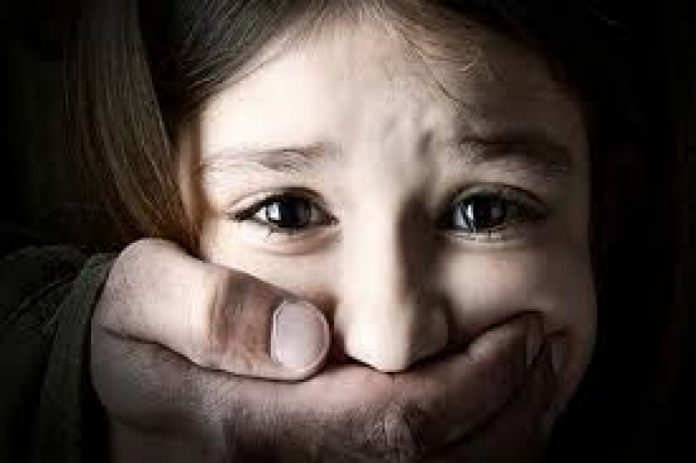 #Pracegover Foto: na imagem há uma menina sendo silenciada pela mão de um adulto