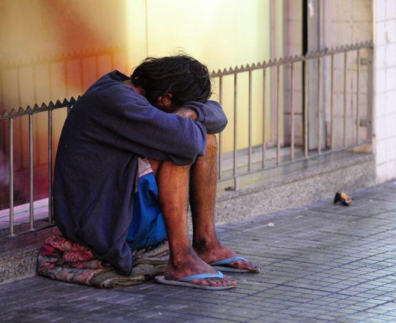 #ParaTodosVerem Na foto, uma pessoa em condição de rua. Ele está sentado em cima de um cobertor com o rosto apoiado sobre os braços