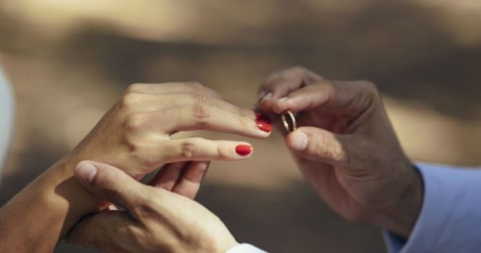 #ParaTodosVerem Na foto, um homem e um mulher com as unhas vermelhas trocam alianças