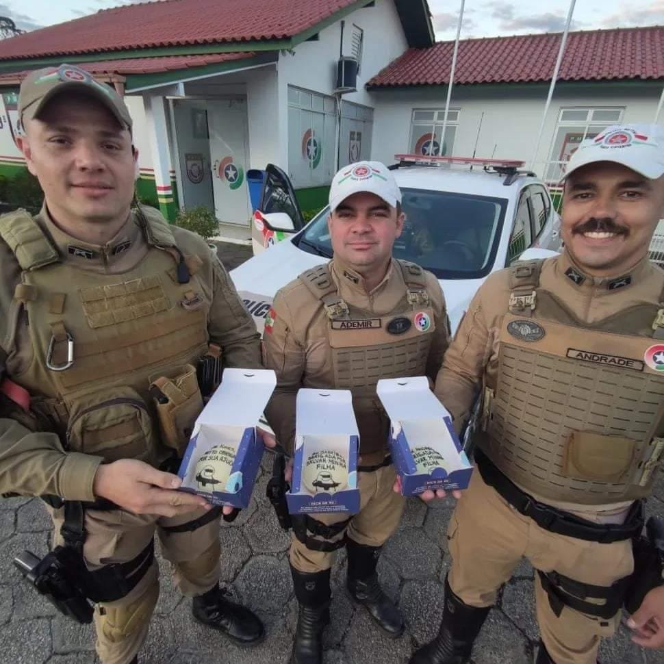 #ParaTodosVerem Na foto, os três policiais militares rodoviários fardados seguram uma caixinha com um bolo