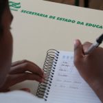 #ParaTodosVerem Na foto, uma criança escreve em um caderno