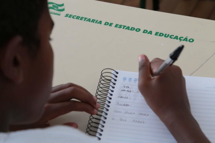 #ParaTodosVerem Na foto, uma criança escreve em um caderno
