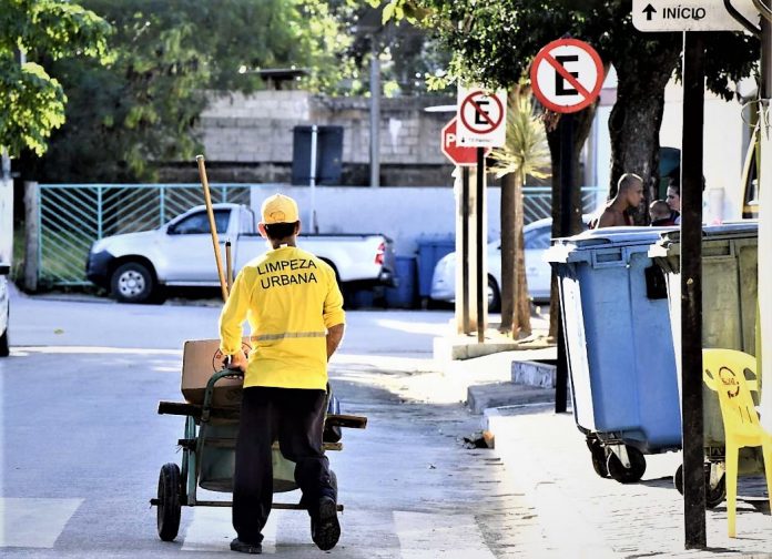 #ParaTodosVerem Na foto, um homem de macacão amarelo, onde está escrito limpeza urbana, caminha em um rua