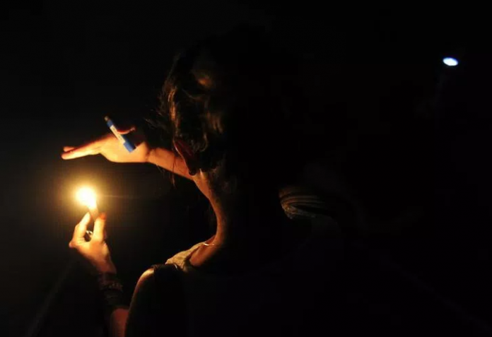 #ParaTodosVerem Na foto, uma mulher caminha no escuro com uma vela na mão