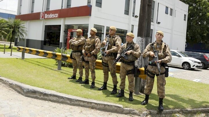 Policiais armados, fardados, formando coluna próximo a agência bancária